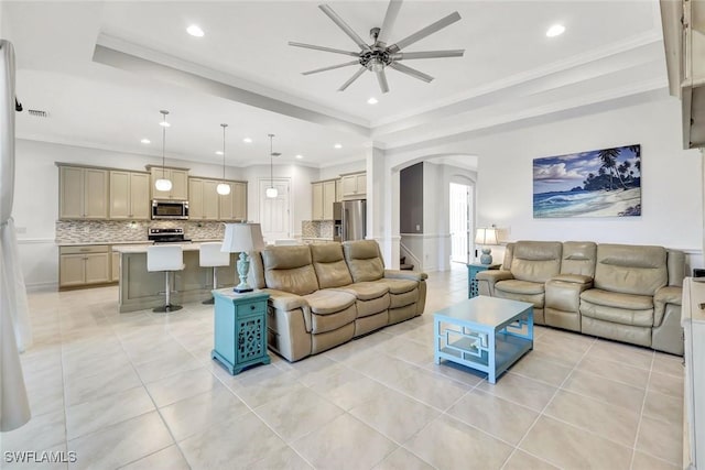 living area with light tile patterned floors, arched walkways, a raised ceiling, a ceiling fan, and ornamental molding