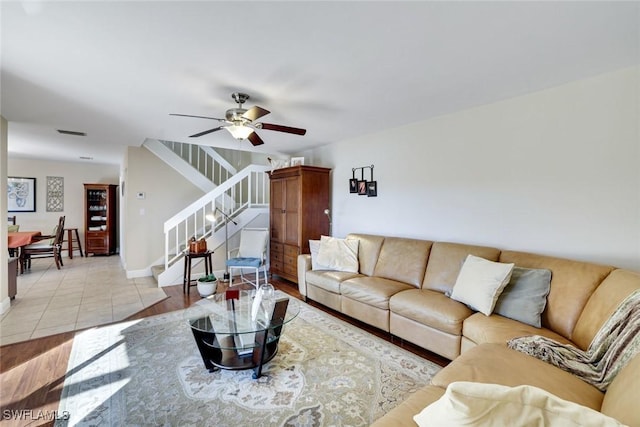 living room with light tile patterned floors, ceiling fan, visible vents, baseboards, and stairway