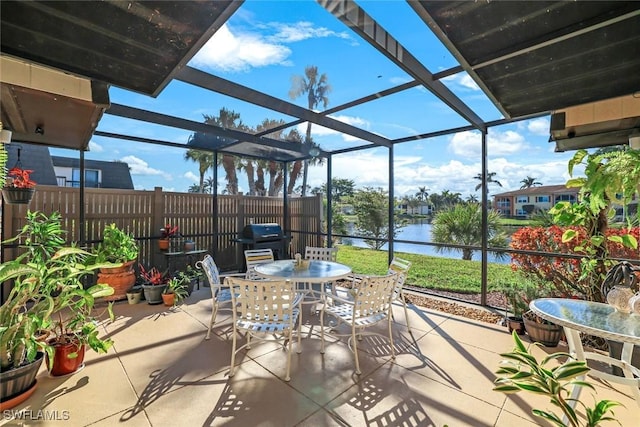 view of patio with outdoor dining area, a water view, a lanai, and fence