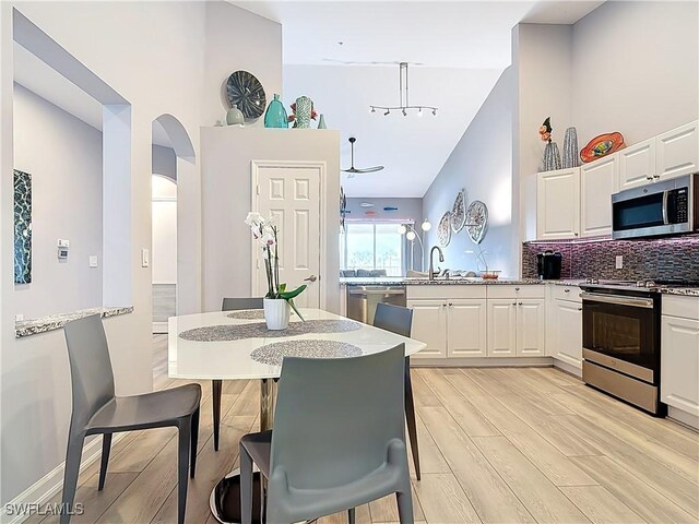 kitchen featuring light stone counters, backsplash, white cabinetry, stainless steel appliances, and light wood finished floors