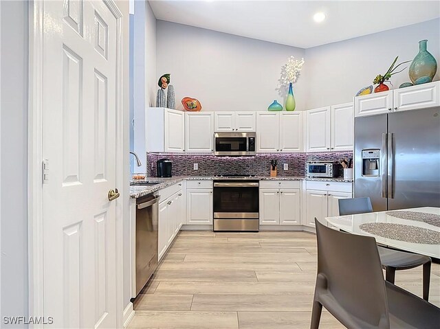 kitchen with a sink, light wood-style floors, appliances with stainless steel finishes, white cabinets, and decorative backsplash