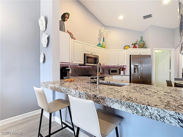 kitchen with visible vents, a kitchen bar, a sink, appliances with stainless steel finishes, and decorative backsplash