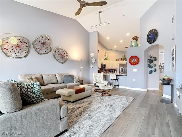 living area with high vaulted ceiling, arched walkways, light wood-style floors, baseboards, and ceiling fan