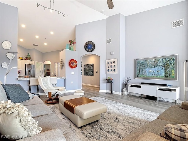 living room featuring visible vents, baseboards, light wood-type flooring, arched walkways, and high vaulted ceiling