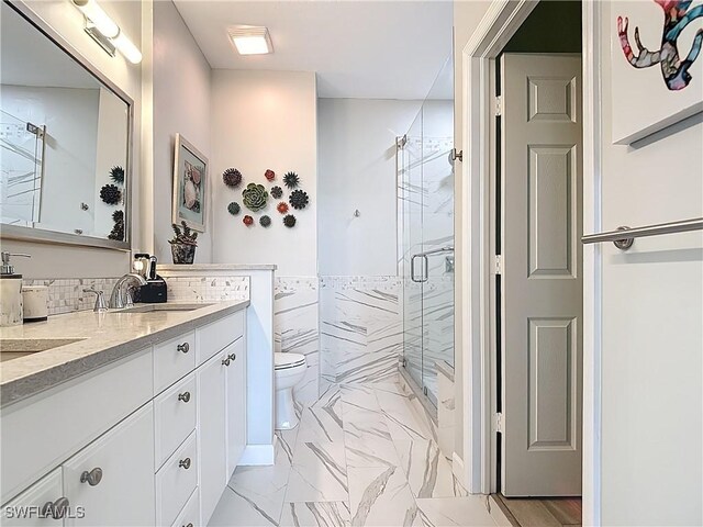 bathroom with a shower stall, toilet, double vanity, marble finish floor, and a sink