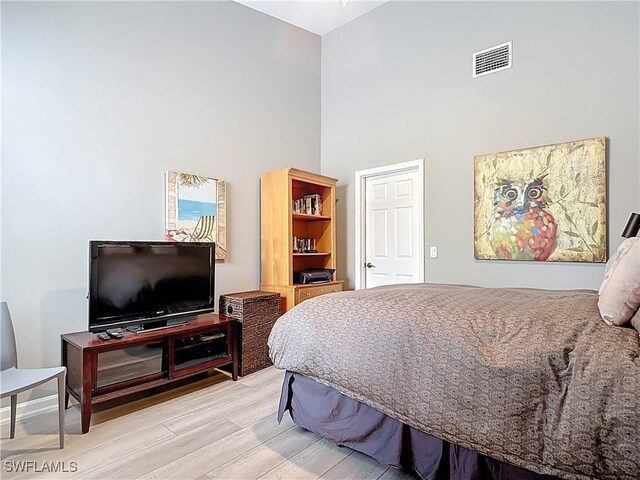 bedroom featuring visible vents, light wood-style flooring, and a high ceiling