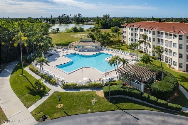 pool with a water view, a patio area, fence, and a lawn