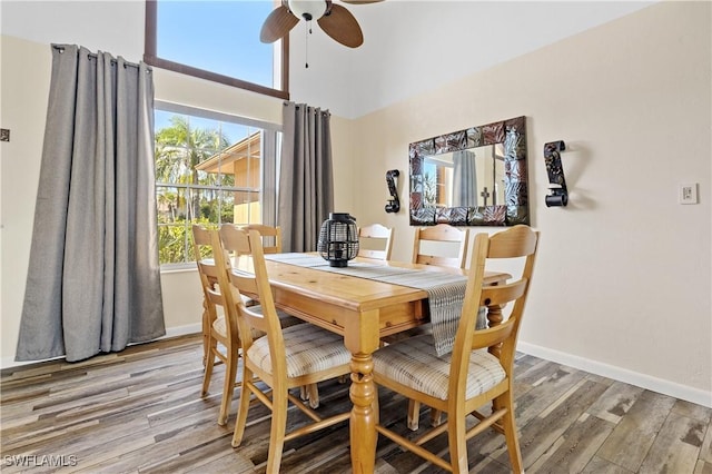 dining room with light wood finished floors, a towering ceiling, a ceiling fan, and baseboards