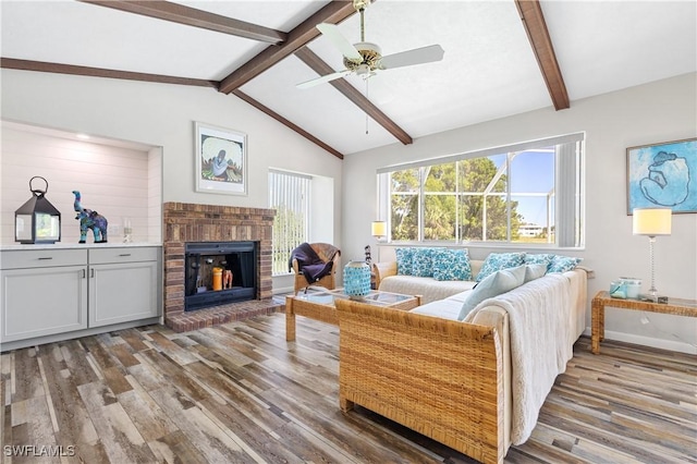 living area with baseboards, lofted ceiling with beams, ceiling fan, wood finished floors, and a brick fireplace