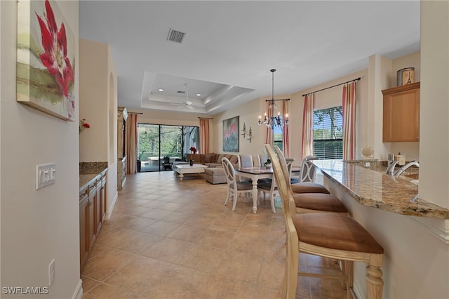 kitchen with ceiling fan with notable chandelier, a raised ceiling, a healthy amount of sunlight, and visible vents