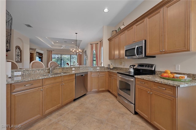 kitchen featuring visible vents, light stone counters, a tray ceiling, a sink, and appliances with stainless steel finishes