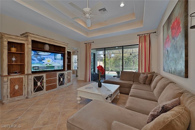 interior space with a tray ceiling, light tile patterned flooring, a ceiling fan, and visible vents