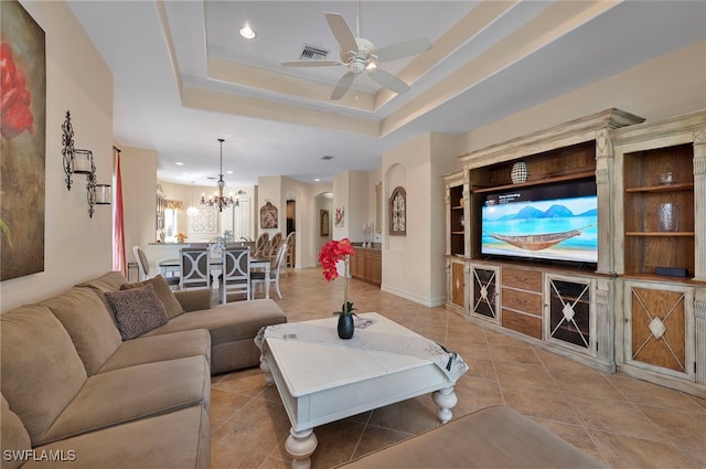 living area with light tile patterned floors, visible vents, a tray ceiling, arched walkways, and ceiling fan with notable chandelier