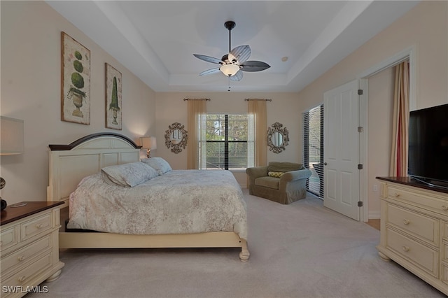 bedroom with light carpet, ceiling fan, and a tray ceiling