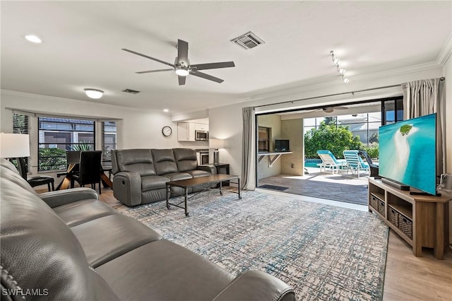 living area with ornamental molding, a ceiling fan, visible vents, and wood finished floors