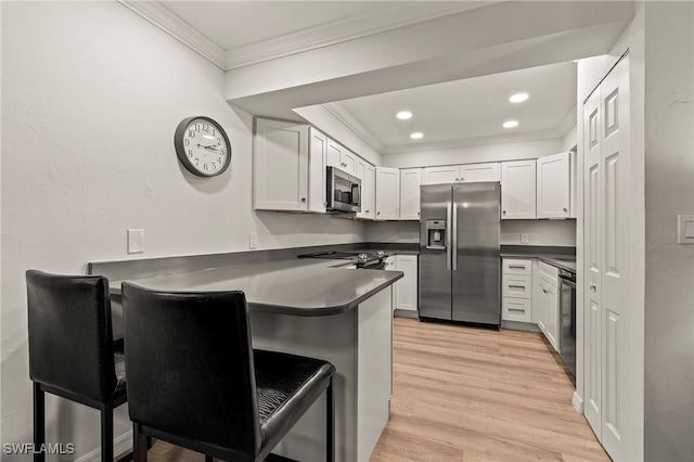 kitchen featuring appliances with stainless steel finishes, dark countertops, crown molding, and a peninsula