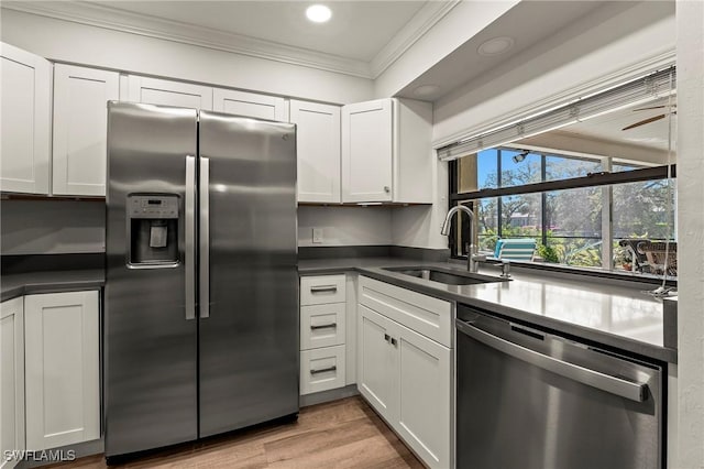 kitchen with crown molding, dark countertops, appliances with stainless steel finishes, white cabinets, and a sink