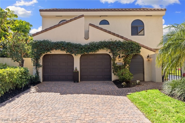 mediterranean / spanish home featuring a garage, decorative driveway, and stucco siding