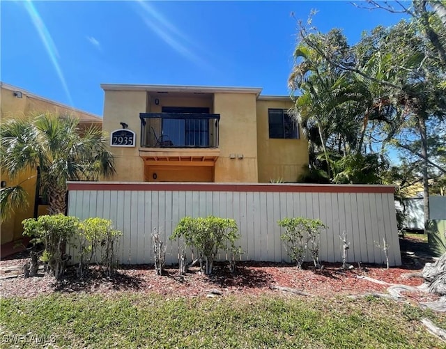 view of front of home featuring a balcony, fence, and stucco siding