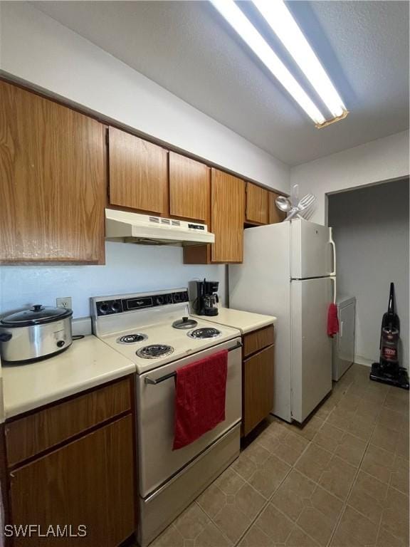 kitchen featuring brown cabinets, white appliances, light countertops, and under cabinet range hood