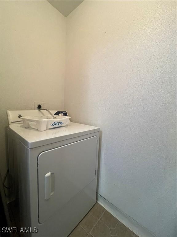 clothes washing area with laundry area, washer / clothes dryer, and dark tile patterned flooring