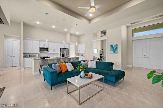 living area with a ceiling fan, baseboards, a high ceiling, and light tile patterned floors