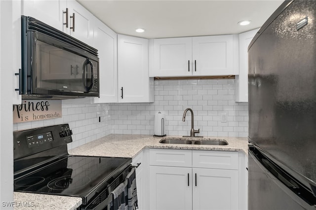 kitchen with a sink, white cabinetry, light stone countertops, black appliances, and tasteful backsplash