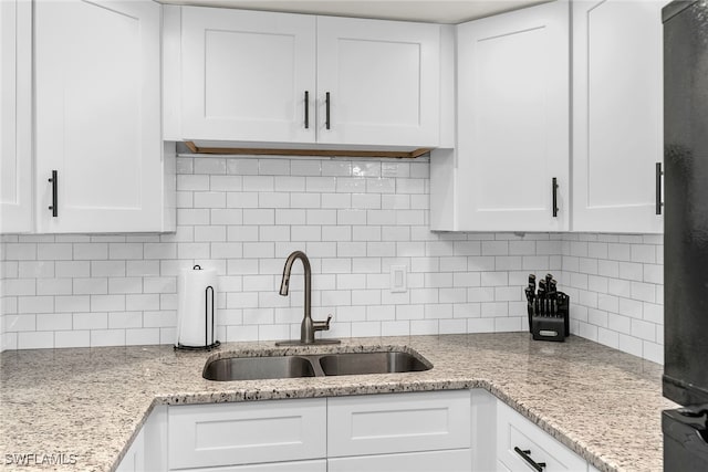 kitchen featuring black refrigerator, a sink, white cabinetry, and decorative backsplash