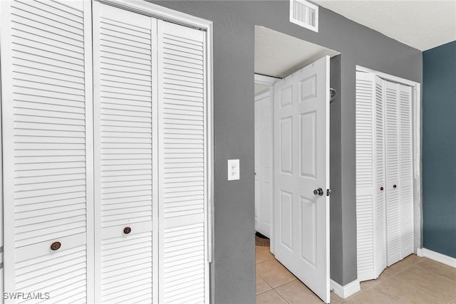 hallway with visible vents, baseboards, and light tile patterned floors