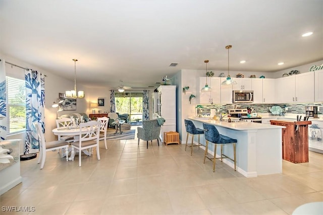 kitchen with light countertops, backsplash, appliances with stainless steel finishes, white cabinets, and a peninsula