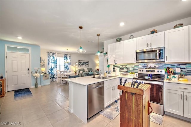 kitchen with stainless steel appliances, a peninsula, a sink, light countertops, and tasteful backsplash