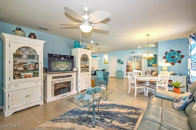 living room featuring ceiling fan with notable chandelier, visible vents, a premium fireplace, and light tile patterned floors