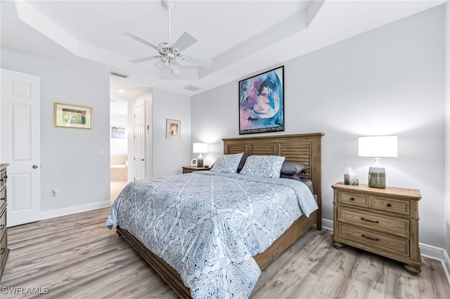 bedroom with light wood finished floors, visible vents, baseboards, and a raised ceiling