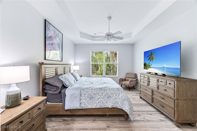 bedroom featuring ceiling fan, a tray ceiling, and light wood-style floors