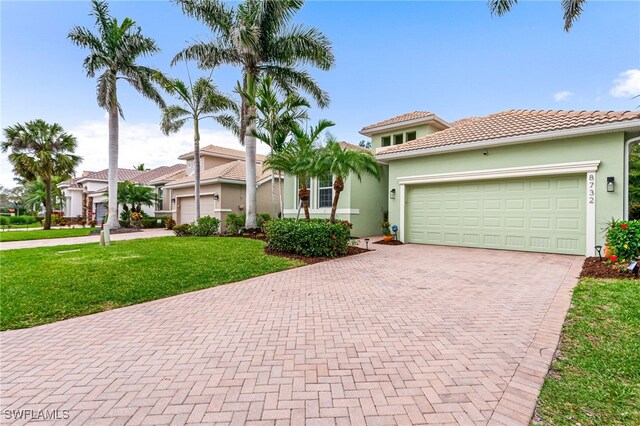 mediterranean / spanish-style house with an attached garage, a tile roof, decorative driveway, stucco siding, and a front lawn