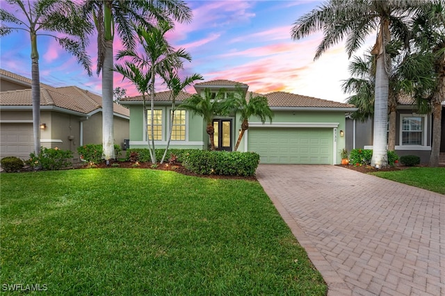 mediterranean / spanish-style home with a front lawn, a tiled roof, stucco siding, decorative driveway, and an attached garage