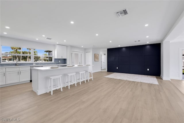 kitchen with light wood-style floors, a breakfast bar, white cabinetry, and visible vents