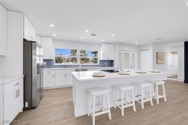 kitchen featuring a kitchen island, a kitchen breakfast bar, white cabinets, appliances with stainless steel finishes, and light wood finished floors