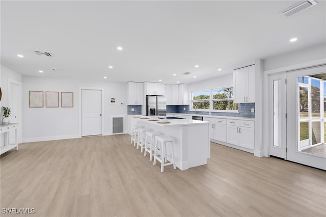 kitchen with a kitchen breakfast bar, stainless steel fridge, visible vents, and light wood-style floors