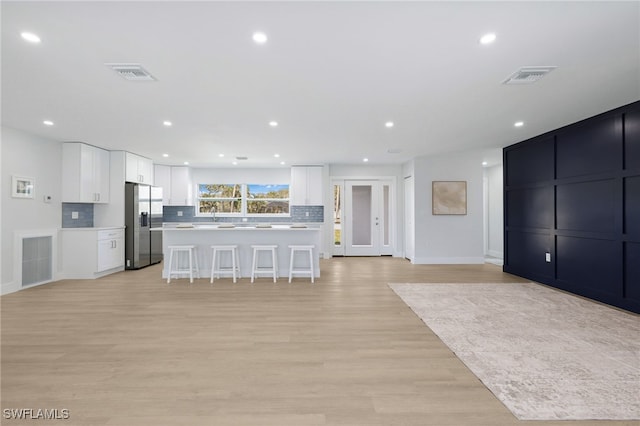 kitchen with a breakfast bar, visible vents, stainless steel refrigerator with ice dispenser, and backsplash