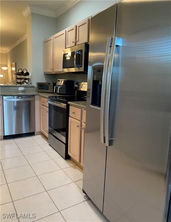 kitchen with light tile patterned floors, stainless steel appliances, dark countertops, and crown molding