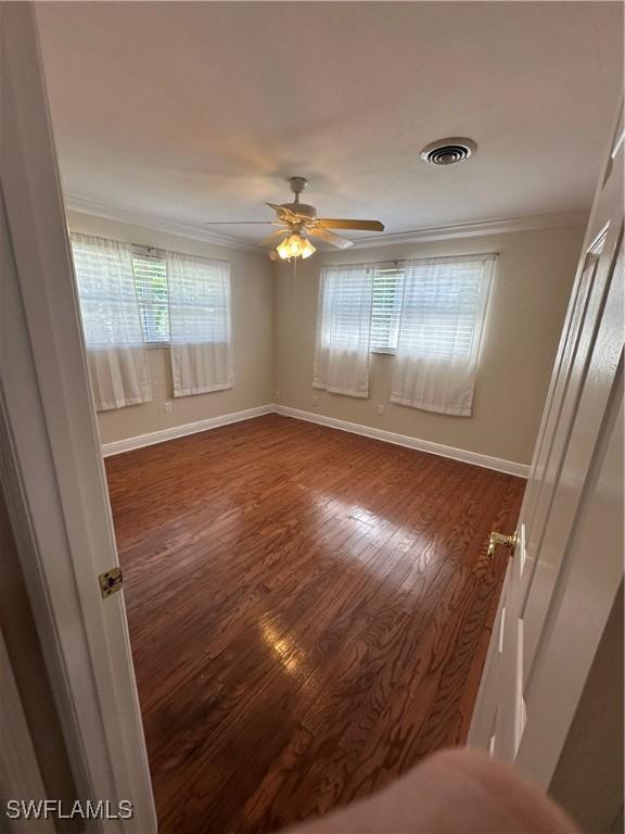 unfurnished room featuring ceiling fan, dark wood-type flooring, visible vents, baseboards, and crown molding