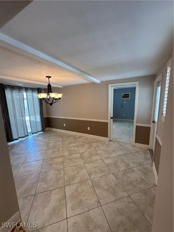 spare room featuring a chandelier, a wealth of natural light, beamed ceiling, and a textured ceiling