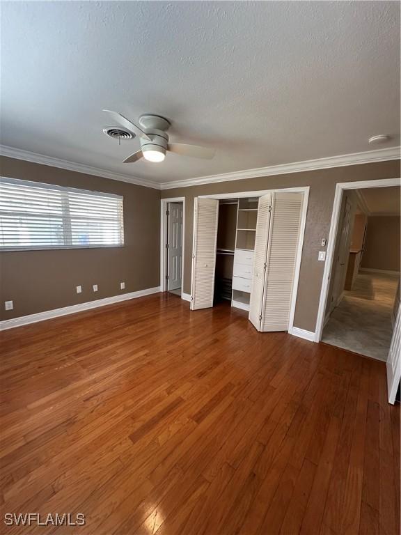 unfurnished bedroom featuring baseboards, visible vents, hardwood / wood-style flooring, ornamental molding, and a textured ceiling