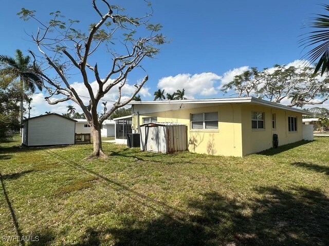 rear view of house with a lawn, an outdoor structure, a sunroom, and central air condition unit