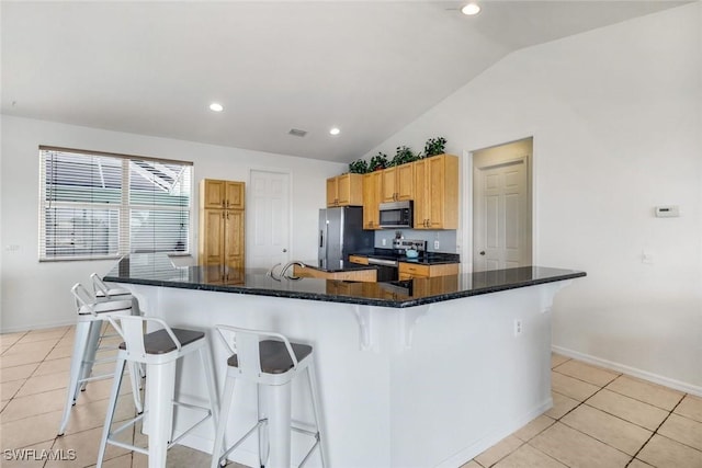 kitchen featuring a kitchen bar, stainless steel appliances, light tile patterned flooring, lofted ceiling, and a large island with sink