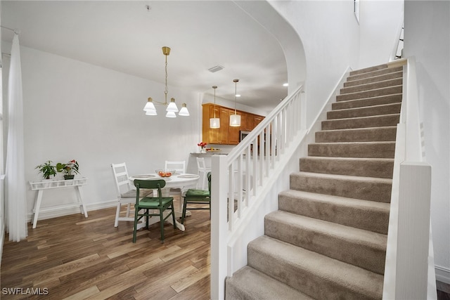 staircase featuring arched walkways, visible vents, wood finished floors, a chandelier, and baseboards