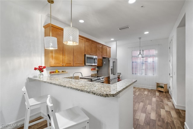 kitchen with visible vents, brown cabinets, a peninsula, stainless steel appliances, and light wood-style floors