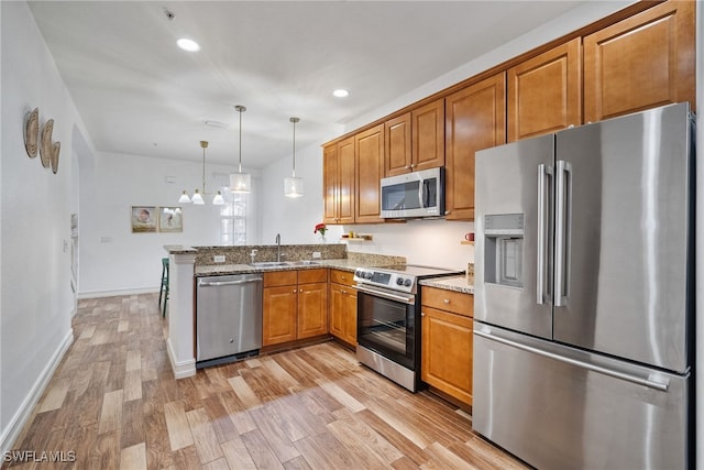 kitchen with stainless steel appliances, light wood-style flooring, brown cabinetry, a sink, and a peninsula