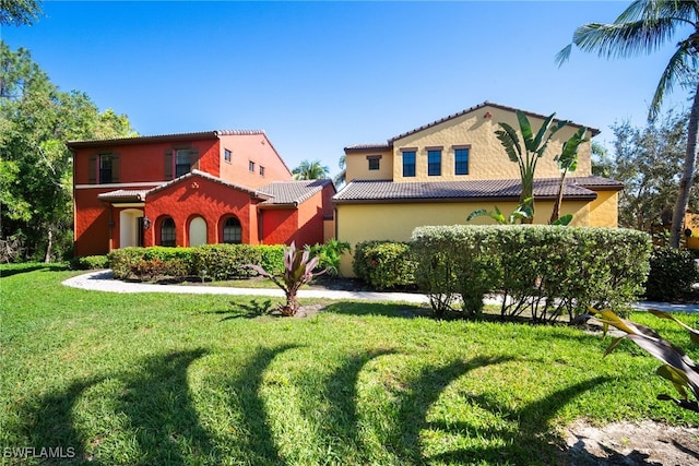 mediterranean / spanish house featuring a front yard, a tile roof, and stucco siding